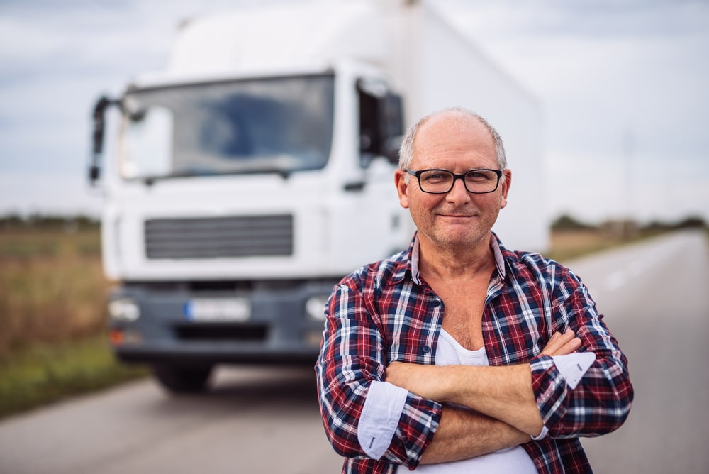 Truck driver posing for the camera with a box truck in the background.