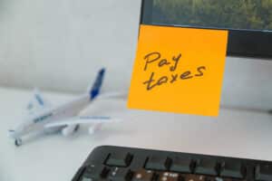 "Pay taxes" written on a sticky note on an expat's desk, with a model airplane in the background.