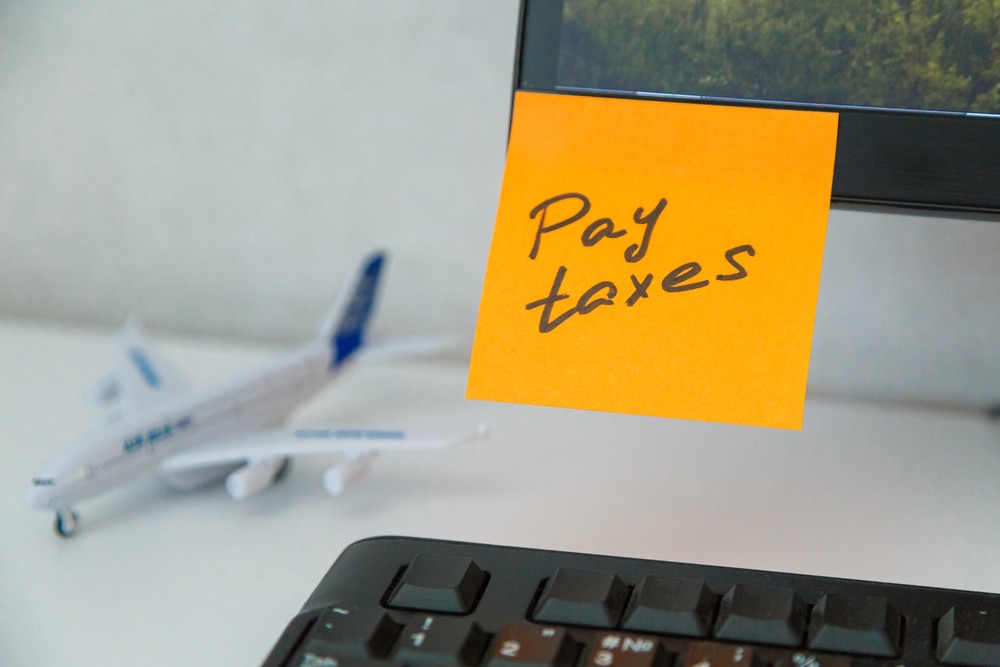 "Pay taxes" written on a sticky note on an expat's desk, with a model airplane in the background.